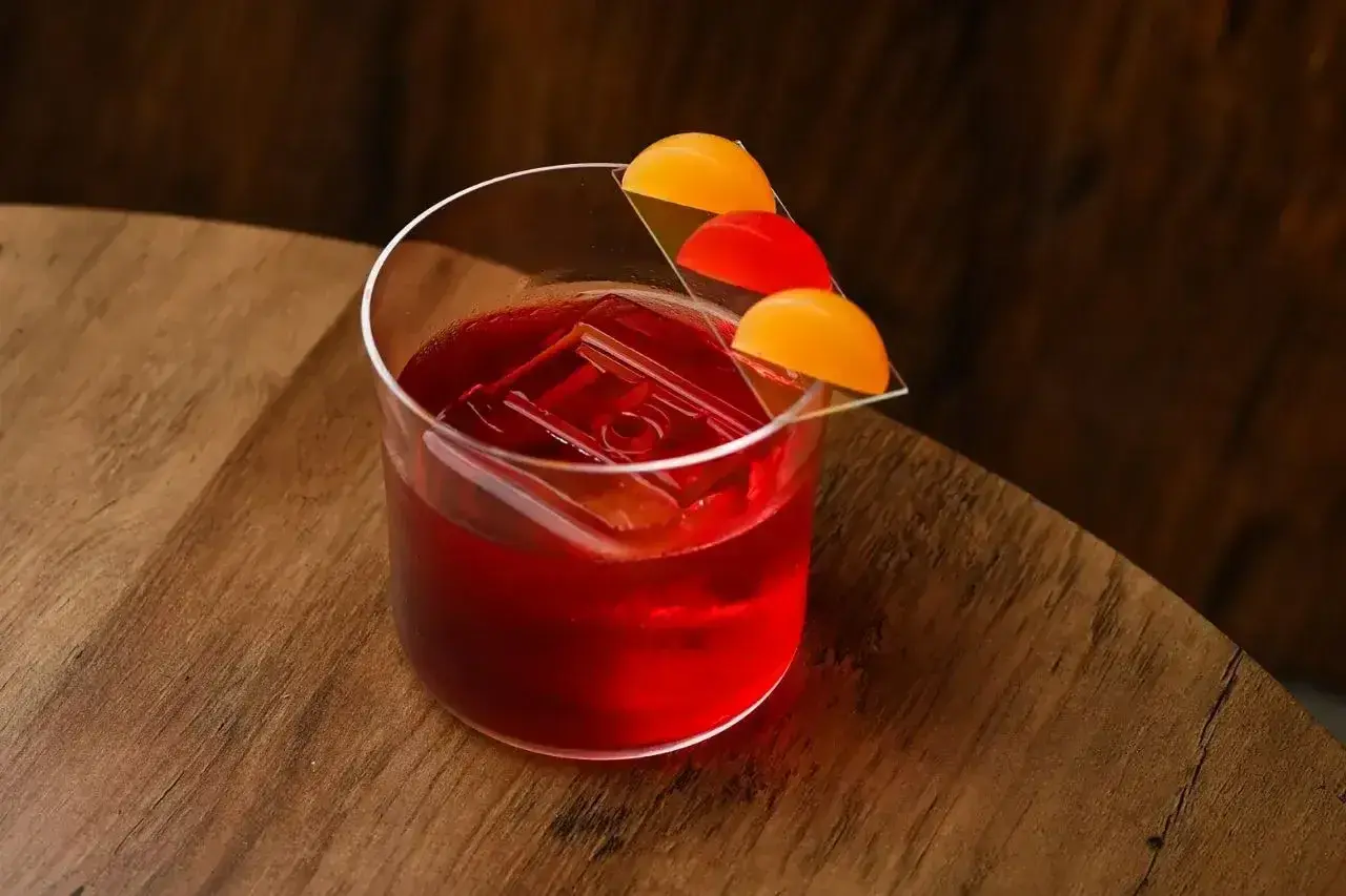Czerwony koktajl Negroni z lodem i plasterkami pomarańczy na szkle.