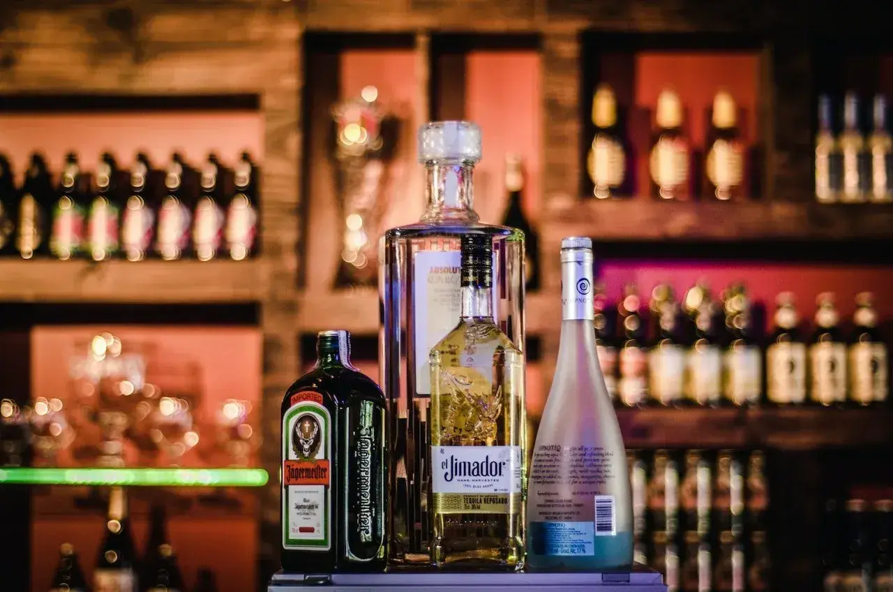 Butelka Jägermeister, Absolut, El Jimador i Hypnotiq. Różne rodzaje alkoholi na półce barowej.