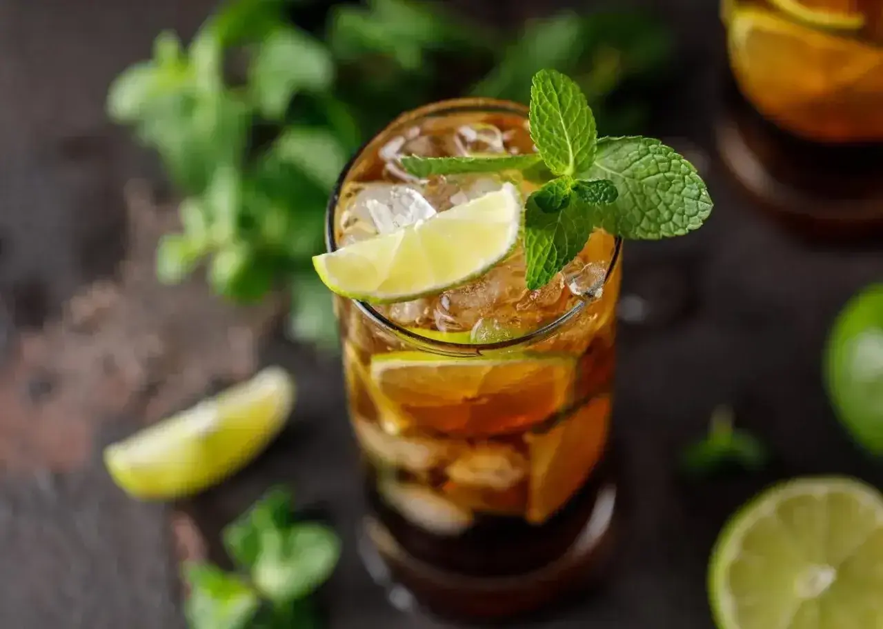 Szklanka z drinkiem Cuba Libre, lodem, plasterkami limonki i listkami mięty.