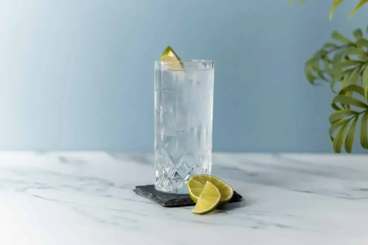 Szklanka z lodem i plasterkami limonki, ozdobiona limonką na brzegu.