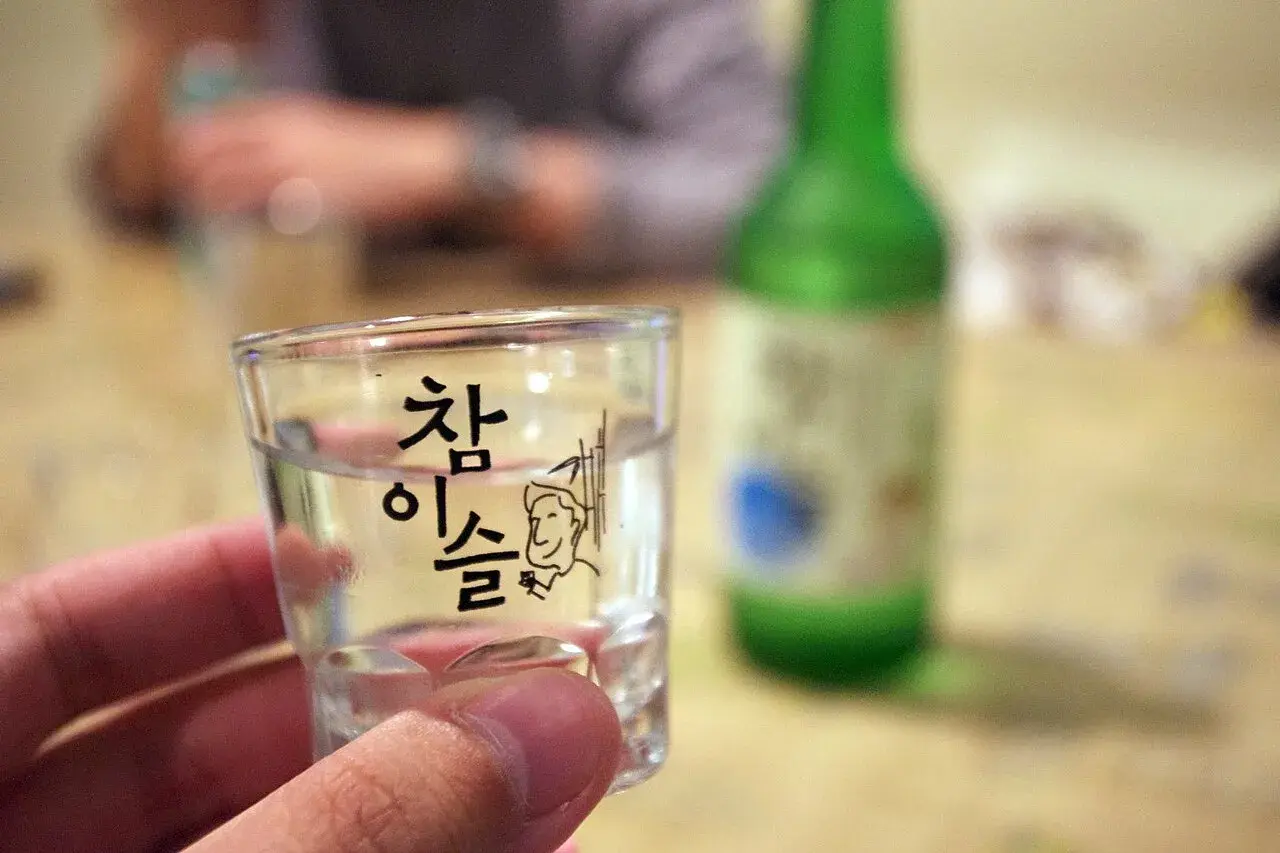 Szklanka z soju z koreańskim napisem i rysunkiem, w tle zielona butelka.