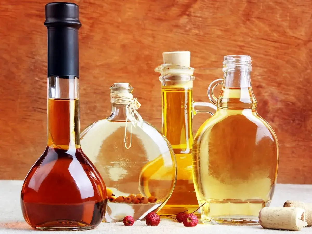 Cztery butelki z płynami: ciemny alkohol, jasny płyn z owocami, złoty olej i miodówka.