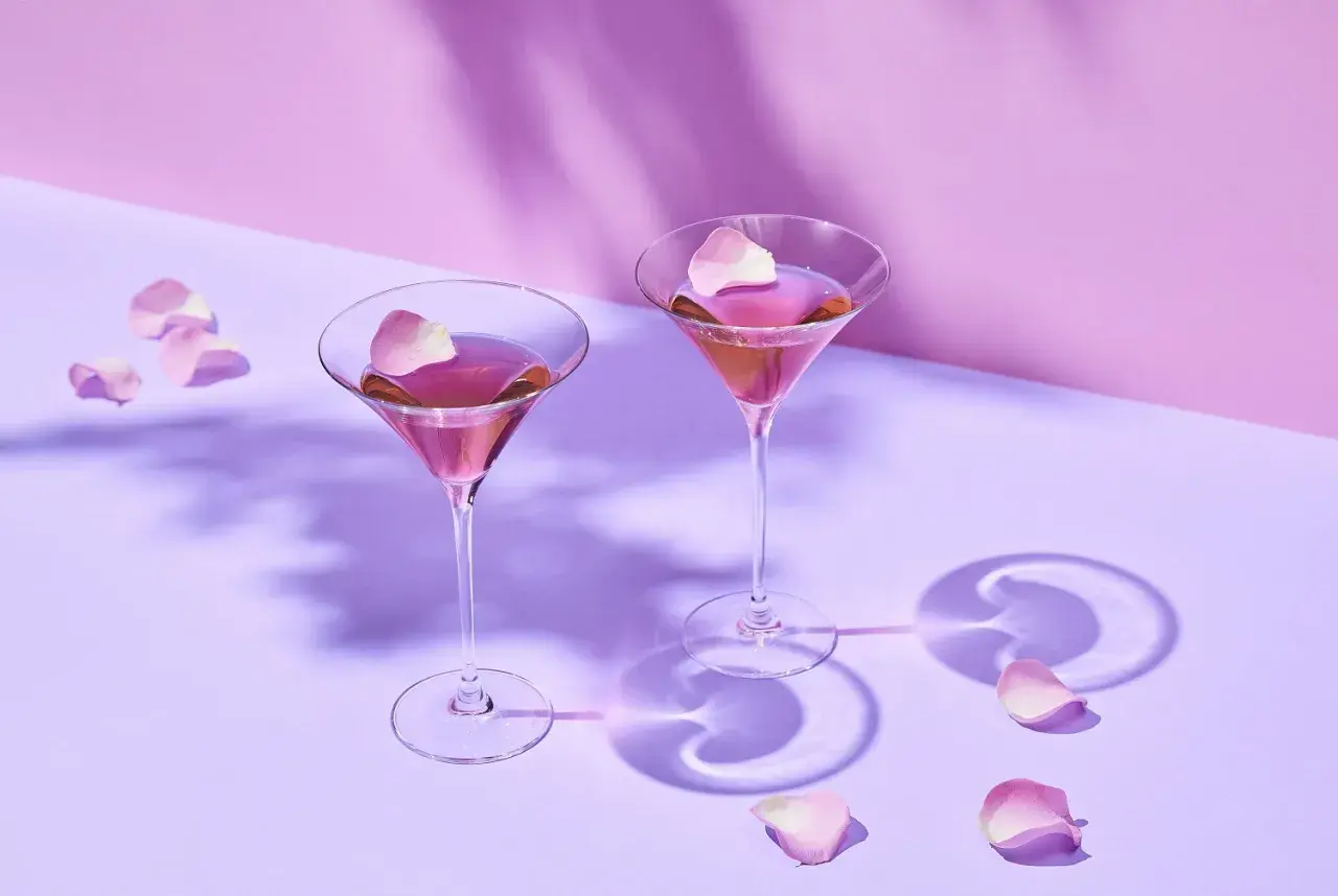 Dwa kieliszki z różowym Martini Rosso, ozdobione płatkami róż. Idealne na romantyczny wieczór. Z czym pić? Z dobrym towarzystwem!