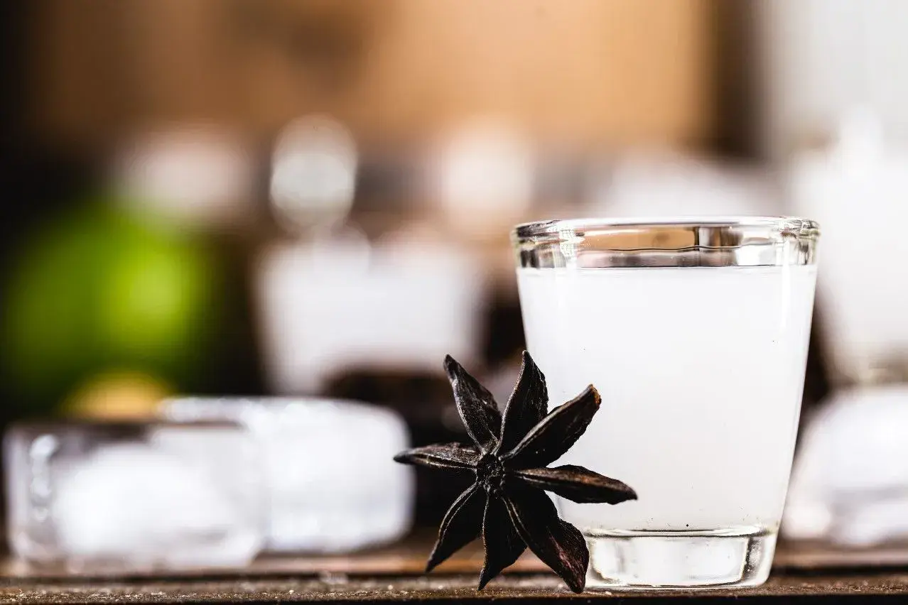 Mętny arak w szklance, obok gwiazdka anyżu i kostki lodu.