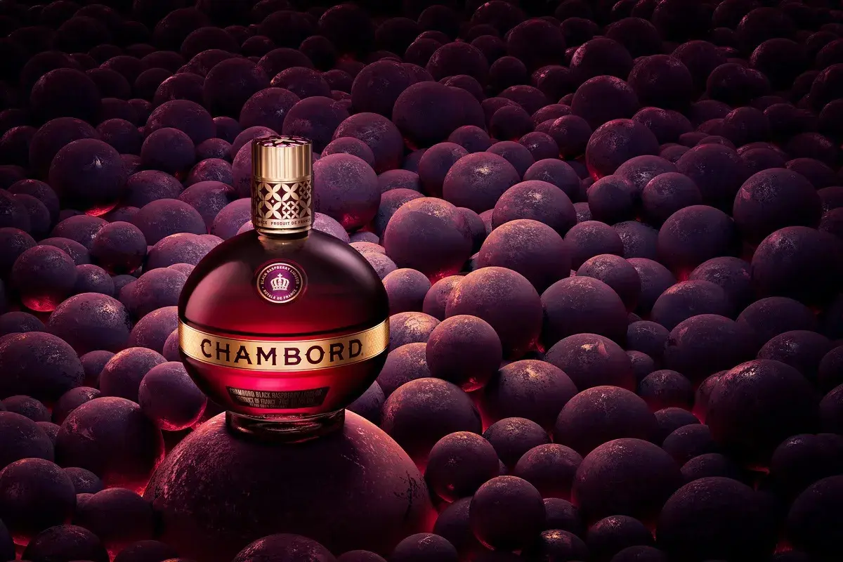 Elegancka butelka likieru Chambord wśród ciemnych, okrągłych owoców, emanująca luksusem i bogactwem smaku.