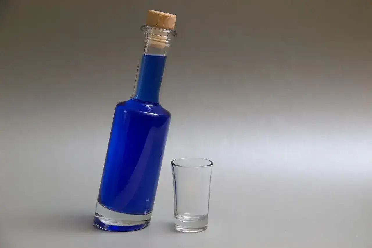 Niebieski likier w butelce z korkiem i pusty kieliszek.