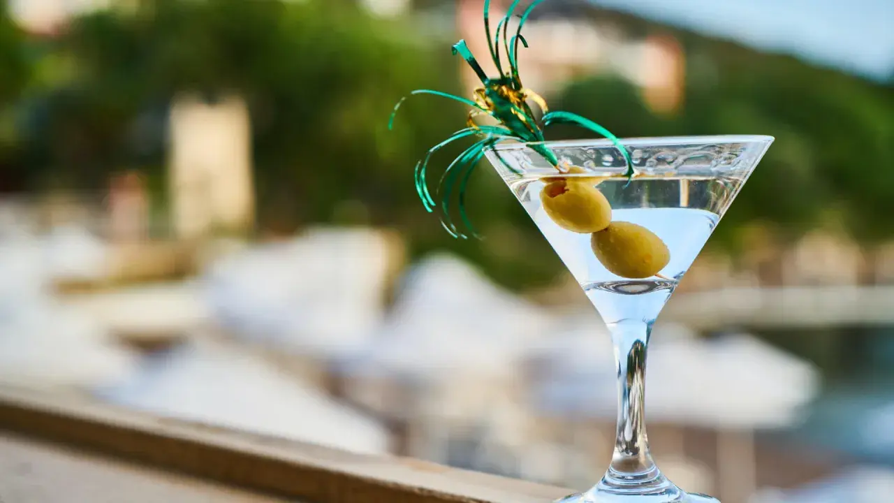 Orzeźwiający martini fiero z oliwkami, ozdobiony zieloną wstążką, na tle rozmytego, letniego krajobrazu.