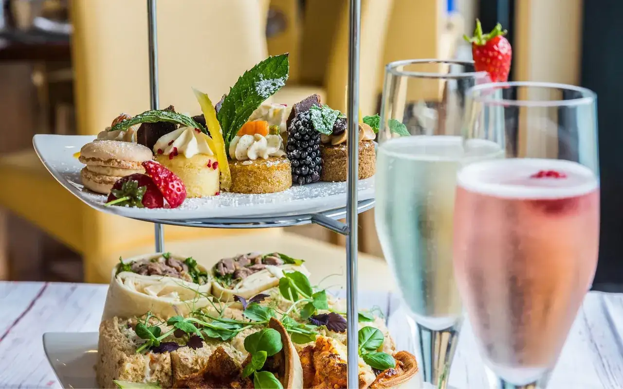 Eleganckie ciastka i makaroniki na piętrowej tacy, idealne do popijania prosecco. Na pierwszym planie dwa kieliszki musującego wina.