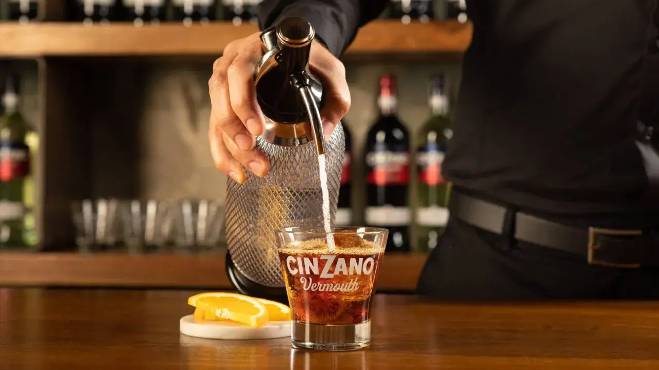 Barman nalewa musujący napój do szklanki z lodem i plasterkiem pomarańczy. Na szkle widnieje napis CINZANO Vermouth.