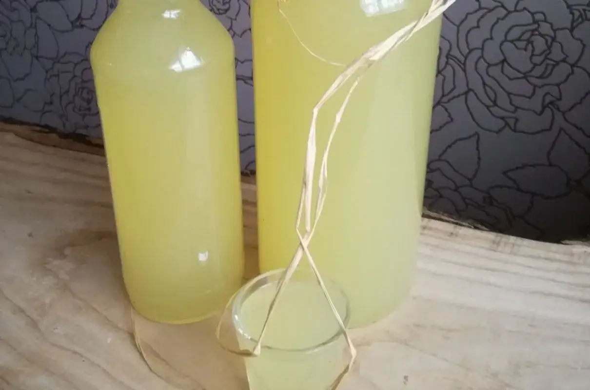 Butelki i kieliszek z domową cytrynówką z miodem, gotową do degustacji.