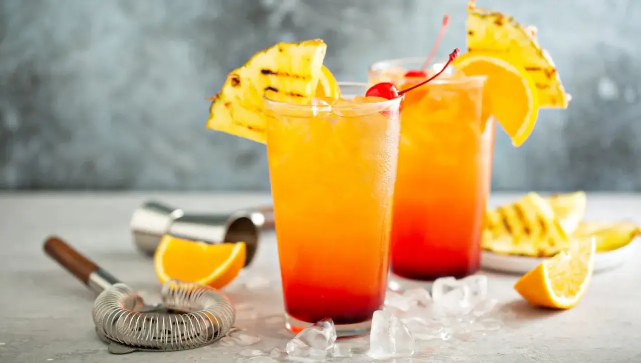 Dwa drinki Tequila Sunrise, ozdobione ananasem i wiśnią. Idealny przepis na lato.