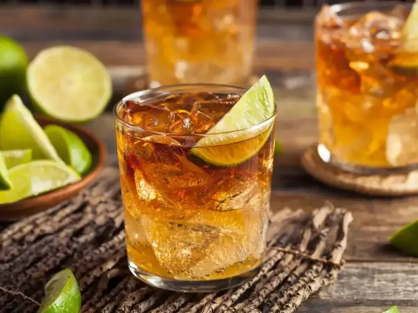 Szklanki z drinkami rumowymi z lodem i limonką, obok miseczka z ćwiartkami limonki.